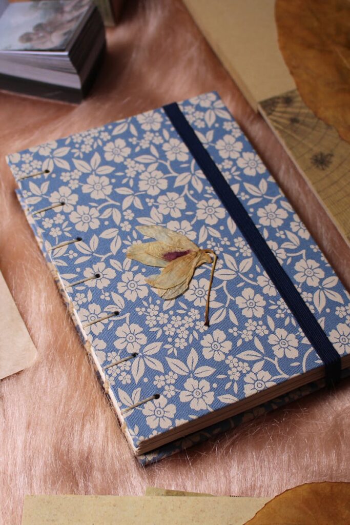 Artistic flat lay of a journal with floral cover, dried leaves, and handwritten letters.